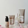 Four skincare products from The Ordinary arranged with pink flower petals on a table