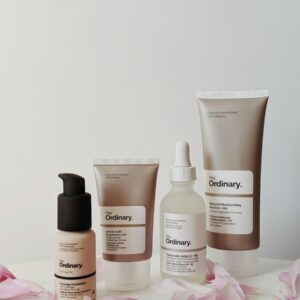 Four skincare products from The Ordinary arranged with pink flower petals on a table