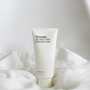 A white tube of body lotion on a soft white fabric surface